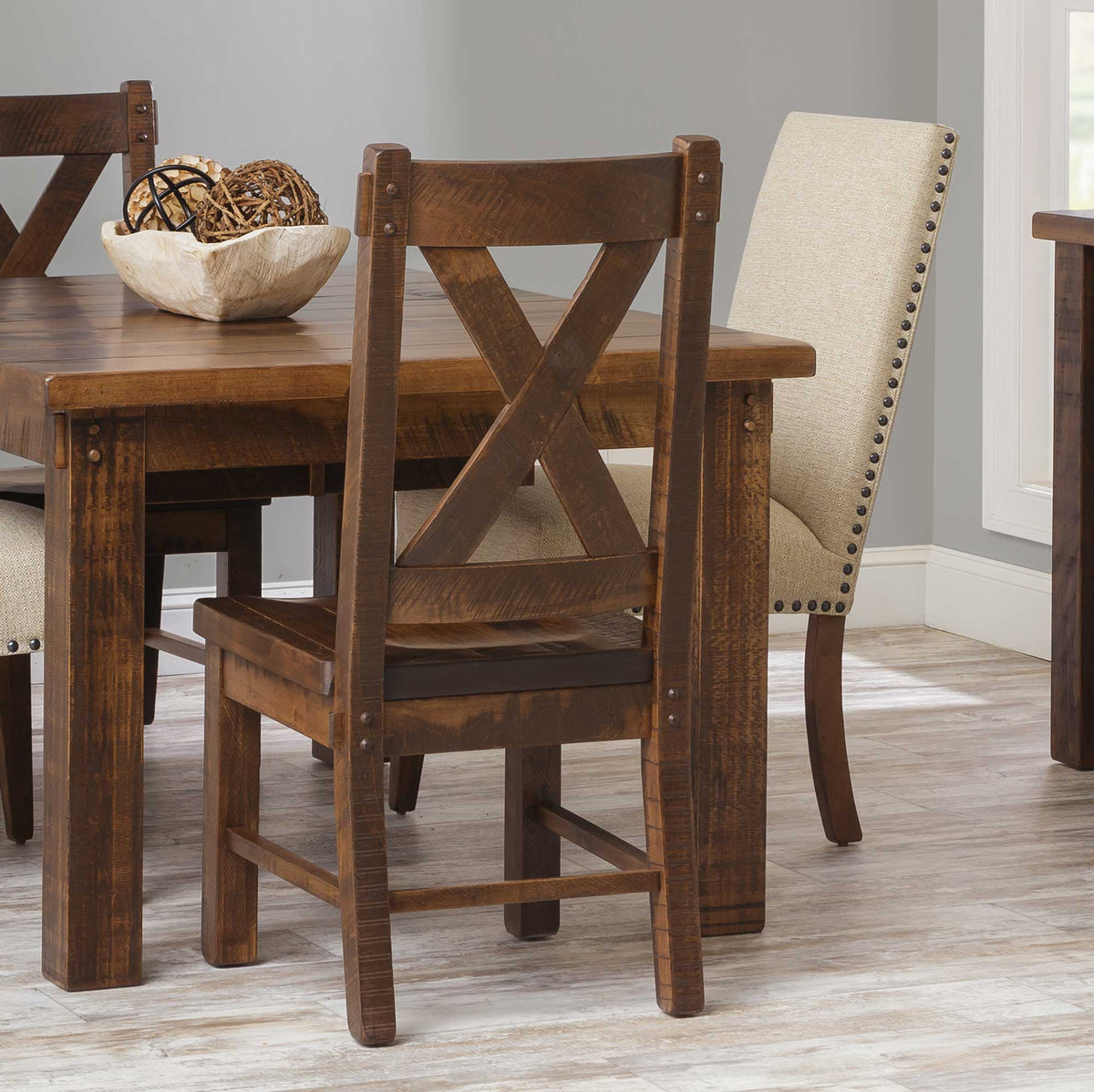 Rustic X back dining chair in distressed brown maple with plank seat and bolt accents at a rough-sawn table
