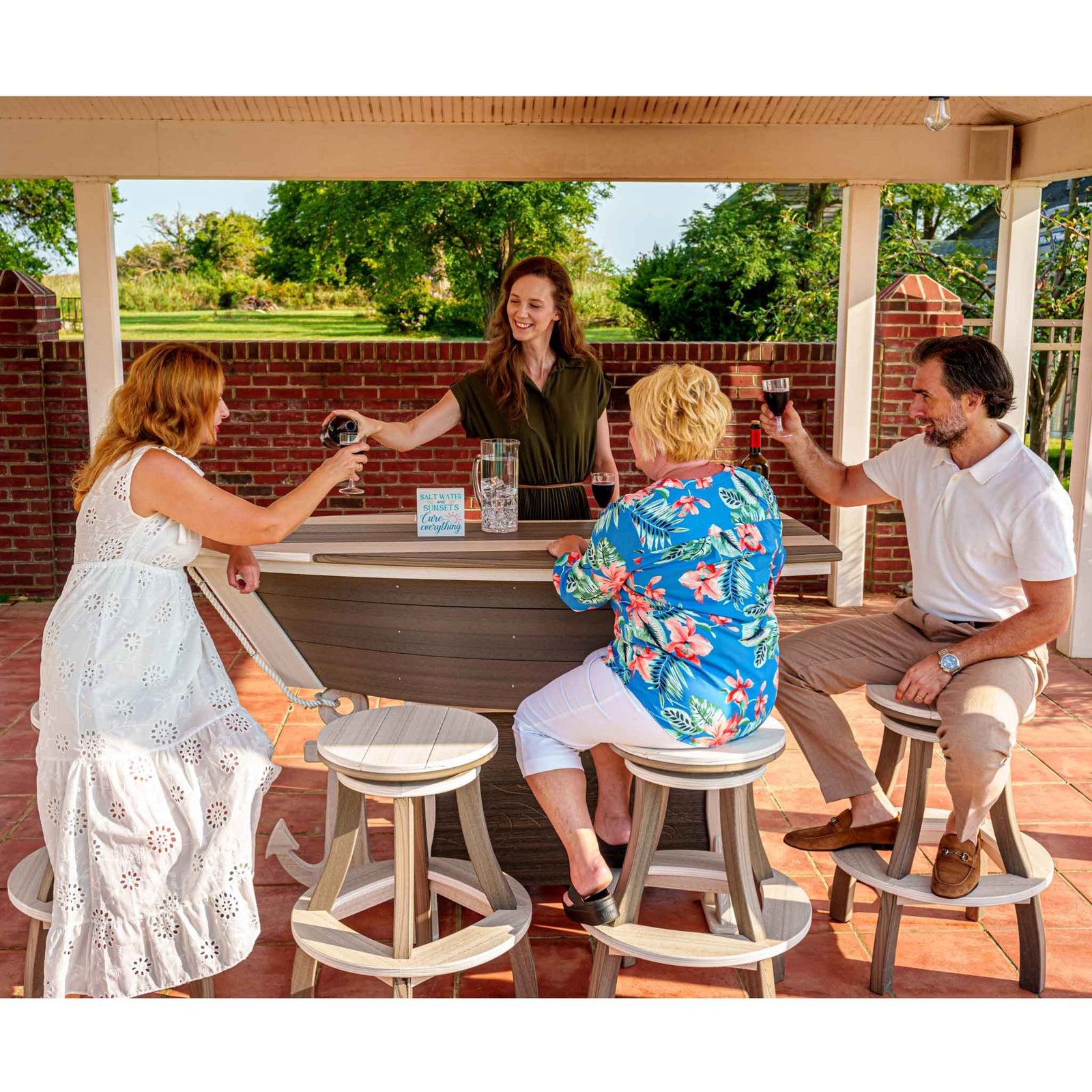 Four people sitting around a boat-shaped bar table with stools, enjoying drinks and having a conversation.