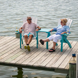 Couple relaxing in white and turquoise poly Adirondack chairs joined by a center table on a lakeside dock