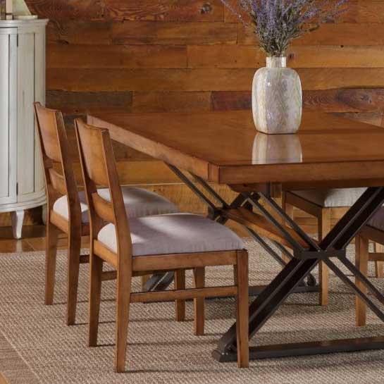 Maple dining table on a black iron X base with modern chairs and gray upholstered seats by a plank wall