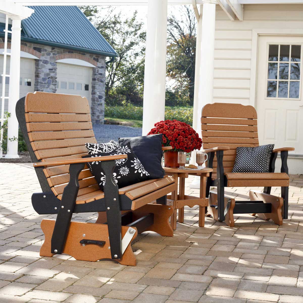 Cedar and black poly patio glider bench and matching glider chair with a small side table on a paver patio by a white porch