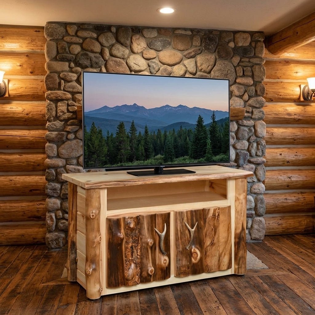 A rustic TV stand made of natural wood logs and branches, holding a large flat-screen TV, set against a stone pillar and log cabin walls.