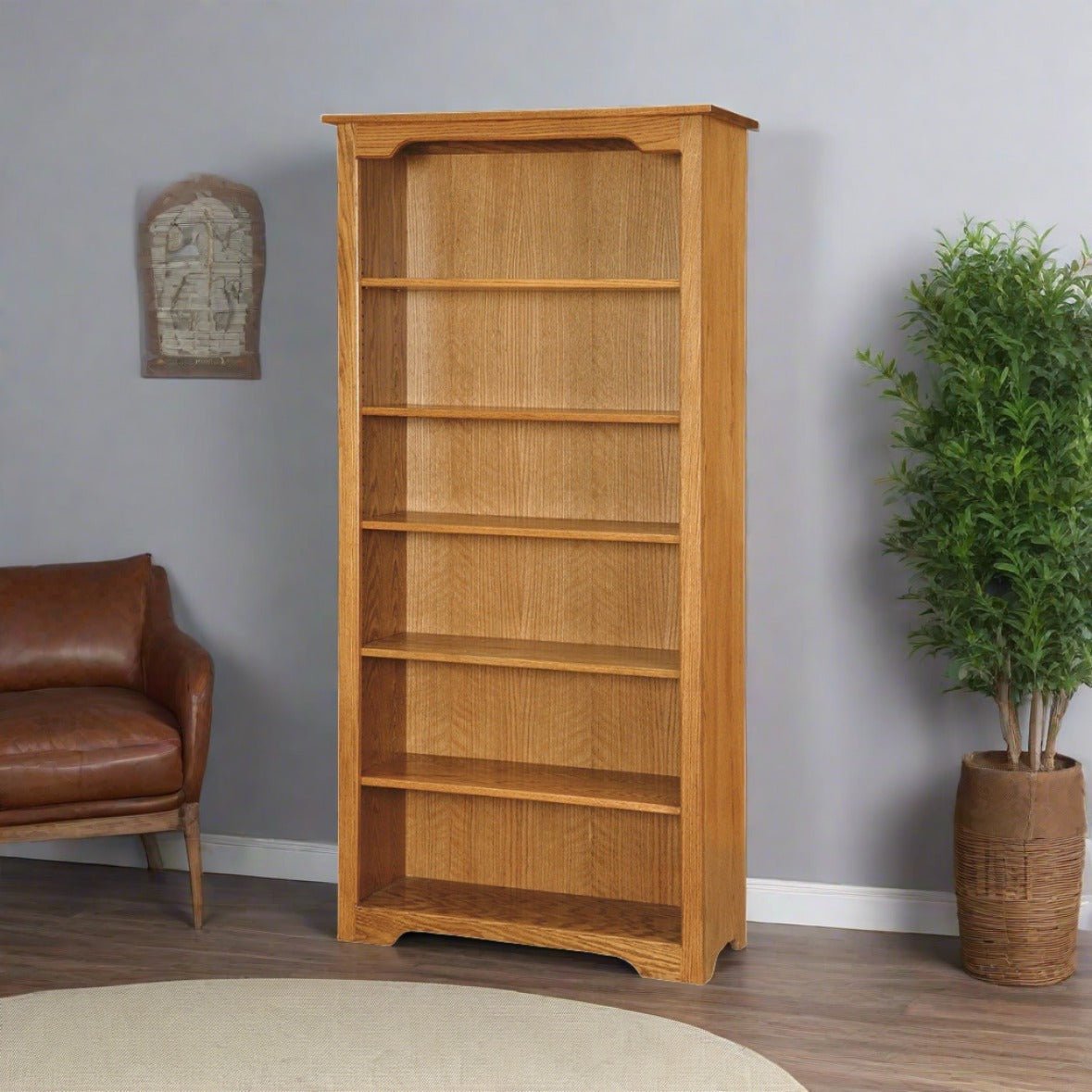 Tall oak bookcase with five adjustable shelves styled in a living room with a leather chair and plant