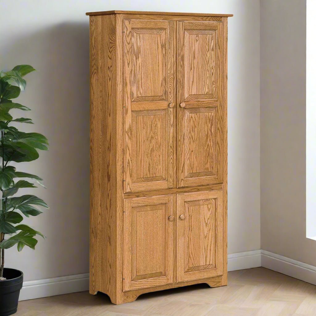 Tall oak storage cabinet with four raised panel doors and round wood knobs standing in a corner beside a plant