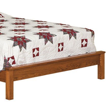 Foot of an oak panel bed showing the low flat footboard rail and square leg with a patchwork quilt
