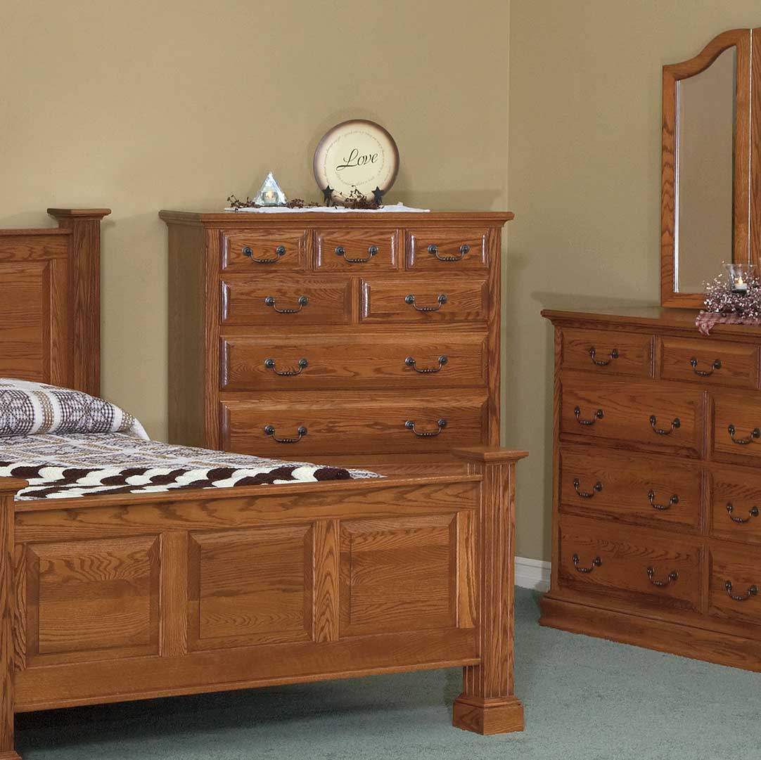 Oak large chest of drawers styled in a bedroom beside a paneled bed and matching mirrored dresser