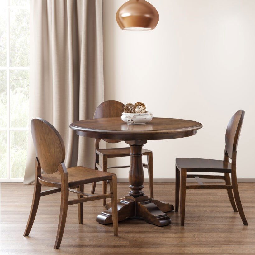 Round pedestal dining table in cherry with three oval back chairs beneath a copper pendant light