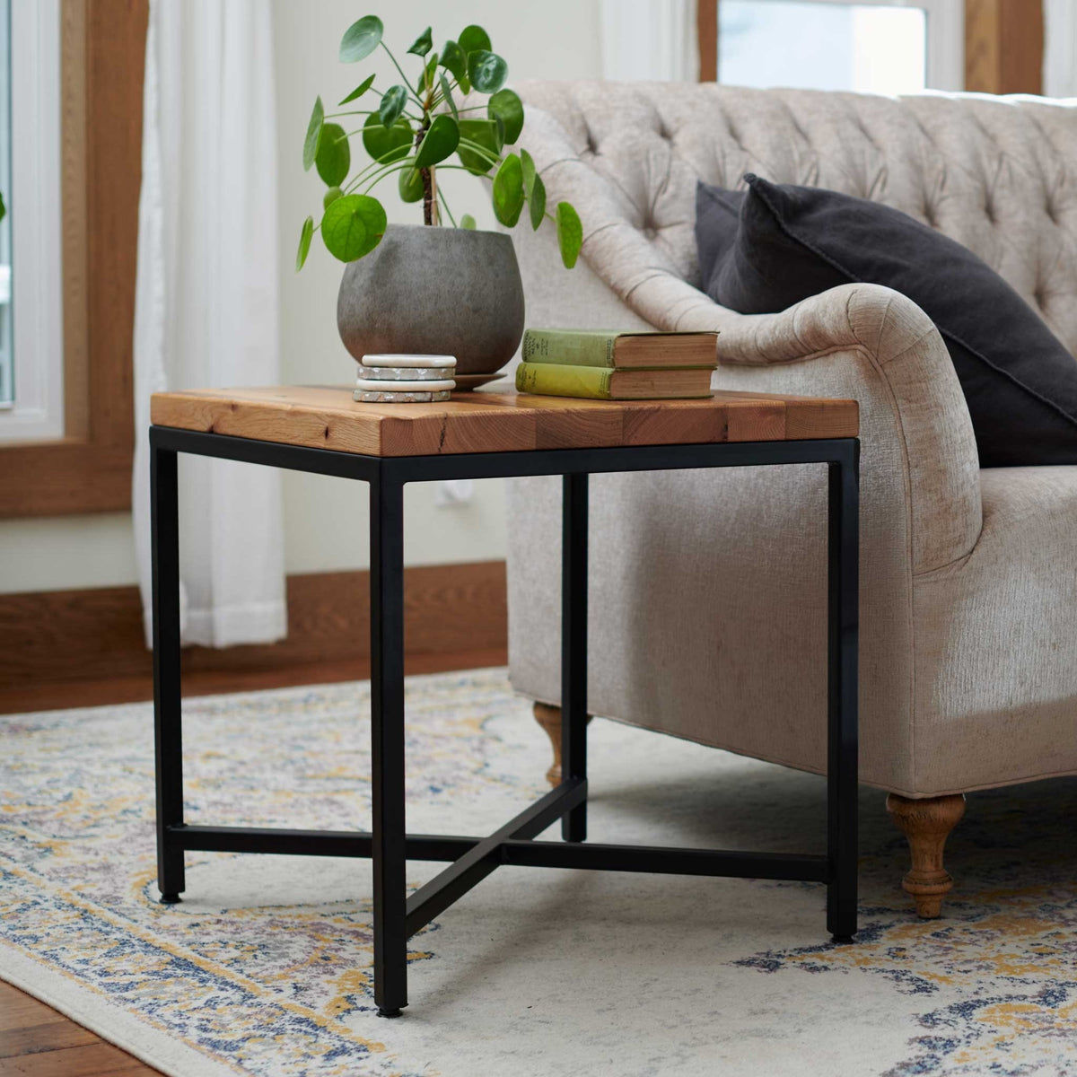 Square end table with a reclaimed wood top on a black steel frame with X stretcher, holding a potted plant and books