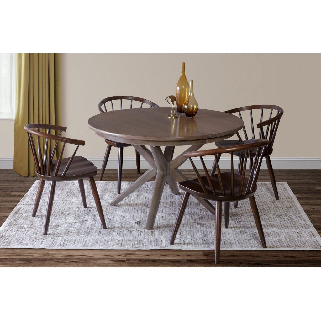 Round pedestal dining table with four curved spindle arm chairs on a patterned rug by a gold curtain