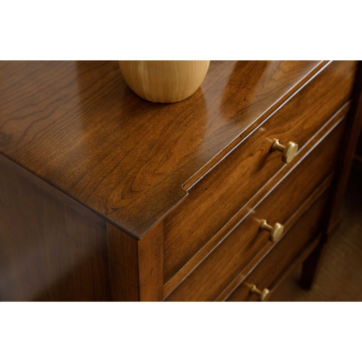 Cherry chest top styled with a light wood vase above three drawers with round brass knob pulls