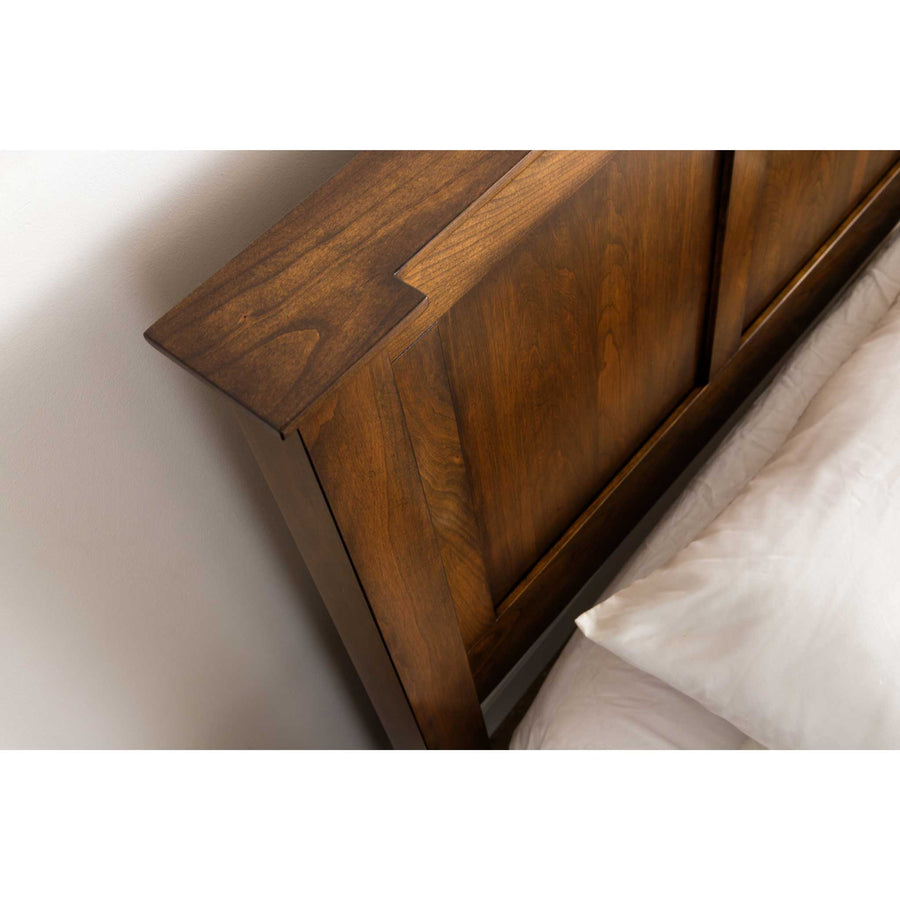 Close-up of a cherry headboard corner showing the stepped crown detail and raised panel construction