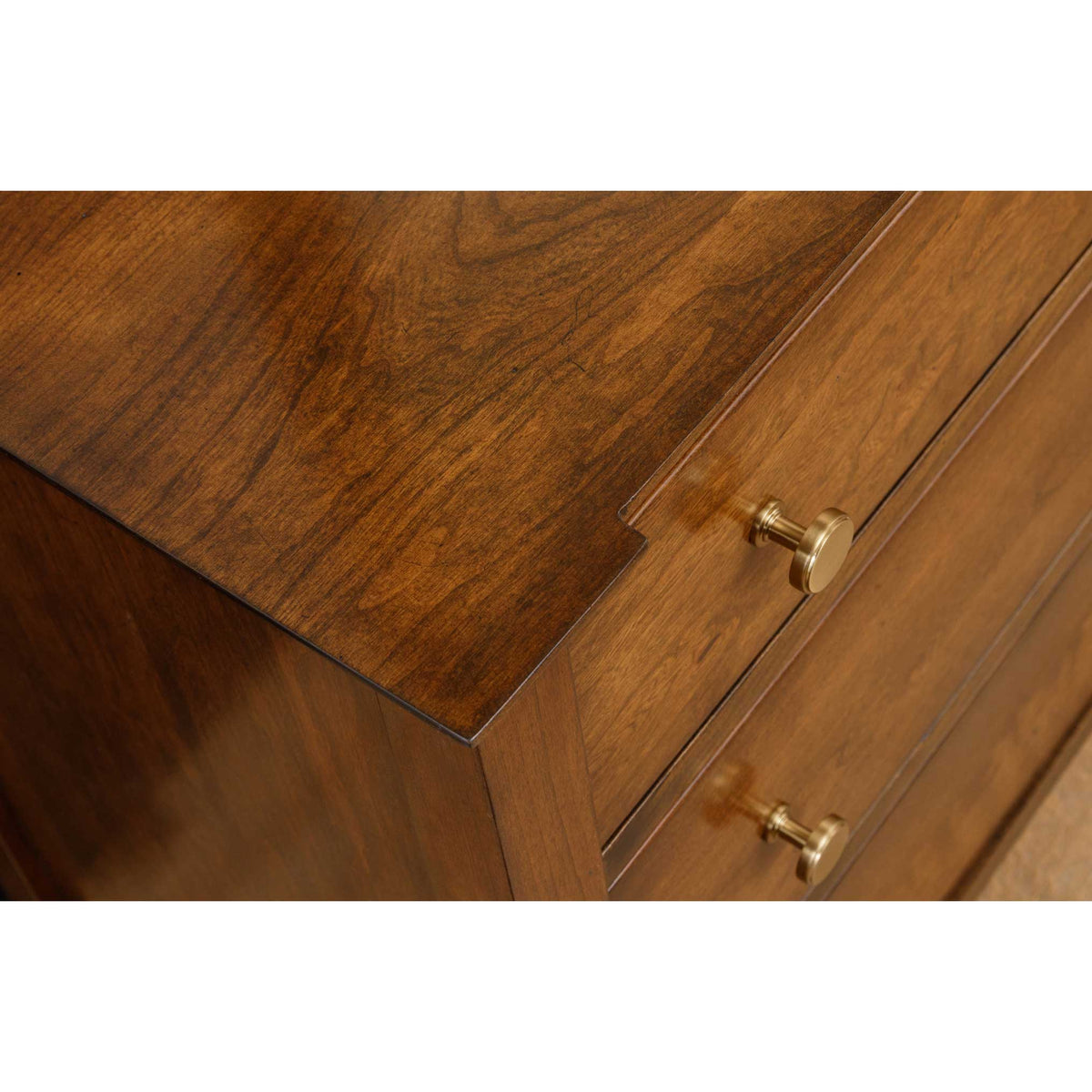 Corner detail of a cherry dresser top with a stepped edge profile and round brass knob drawer pulls