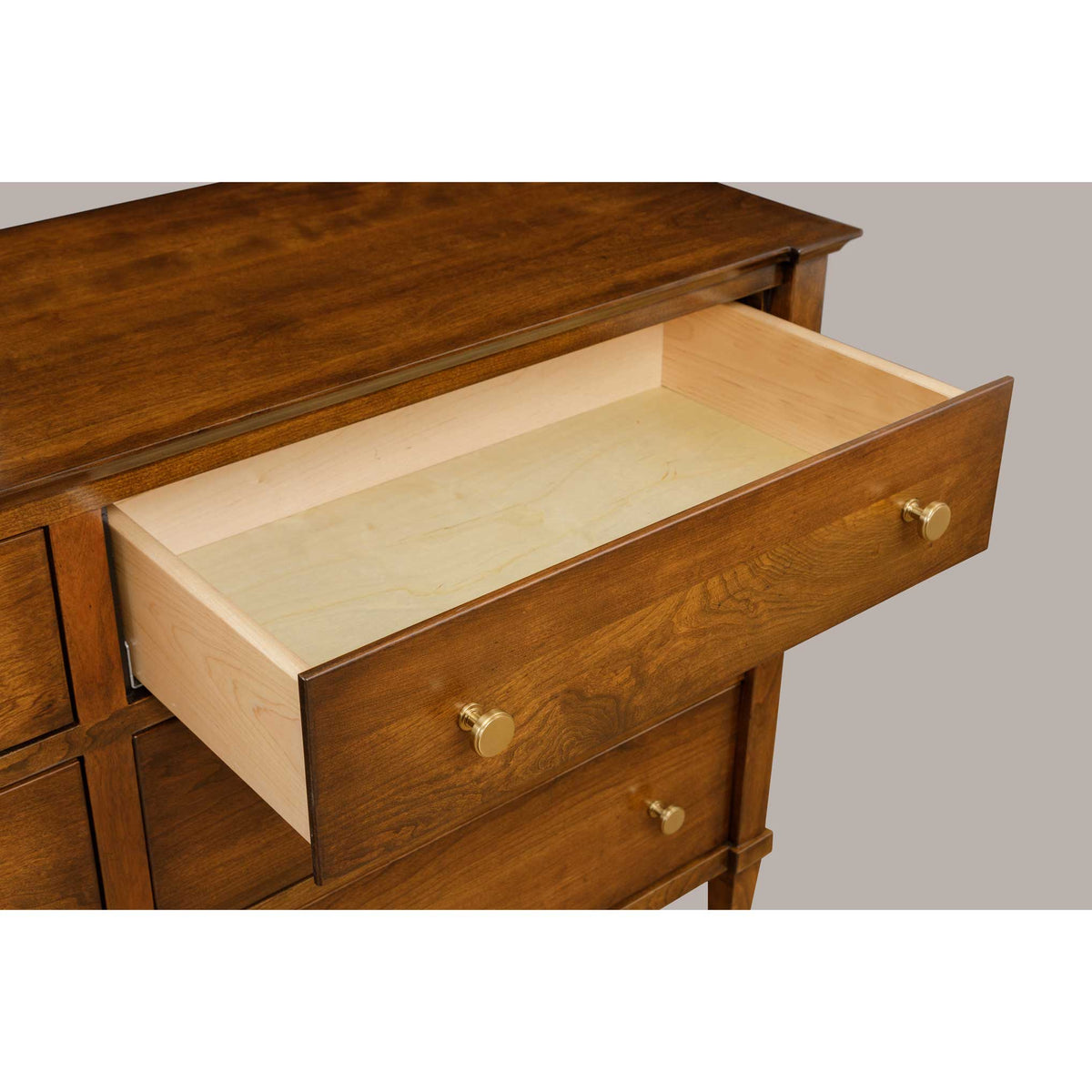 Cherry dresser with one drawer pulled open showing the pale maple drawer box and brass knob pulls