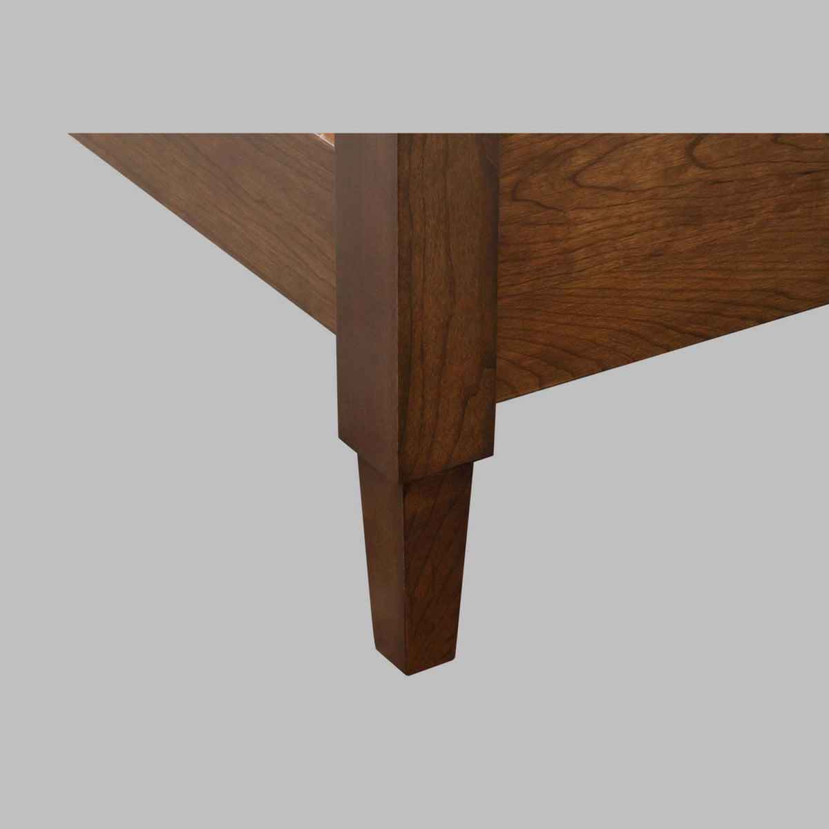 Corner detail of a cherry bed frame showing the side rail meeting a square tapered post foot