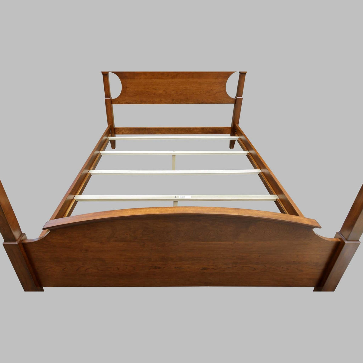 Four poster bed viewed from the foot, showing maple slats, center supports and the arched footboard