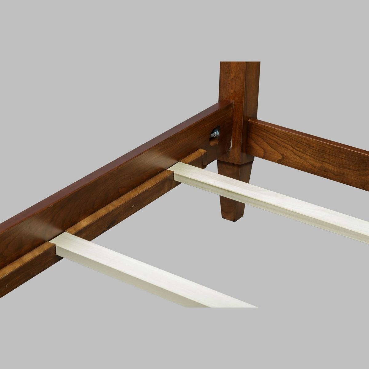 Bed rail and post joint detail with a hex bolt fastener and pale maple slats resting on the ledge