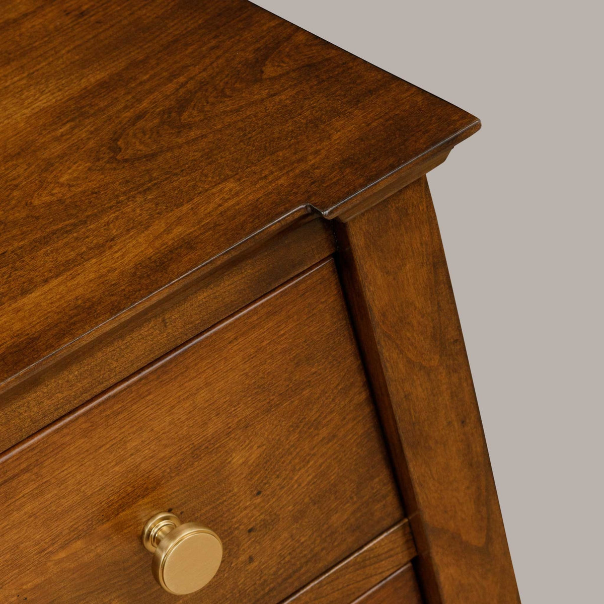 Angled detail of the nightstand's cherry top overhang and beveled edge above a brass-knobbed drawer