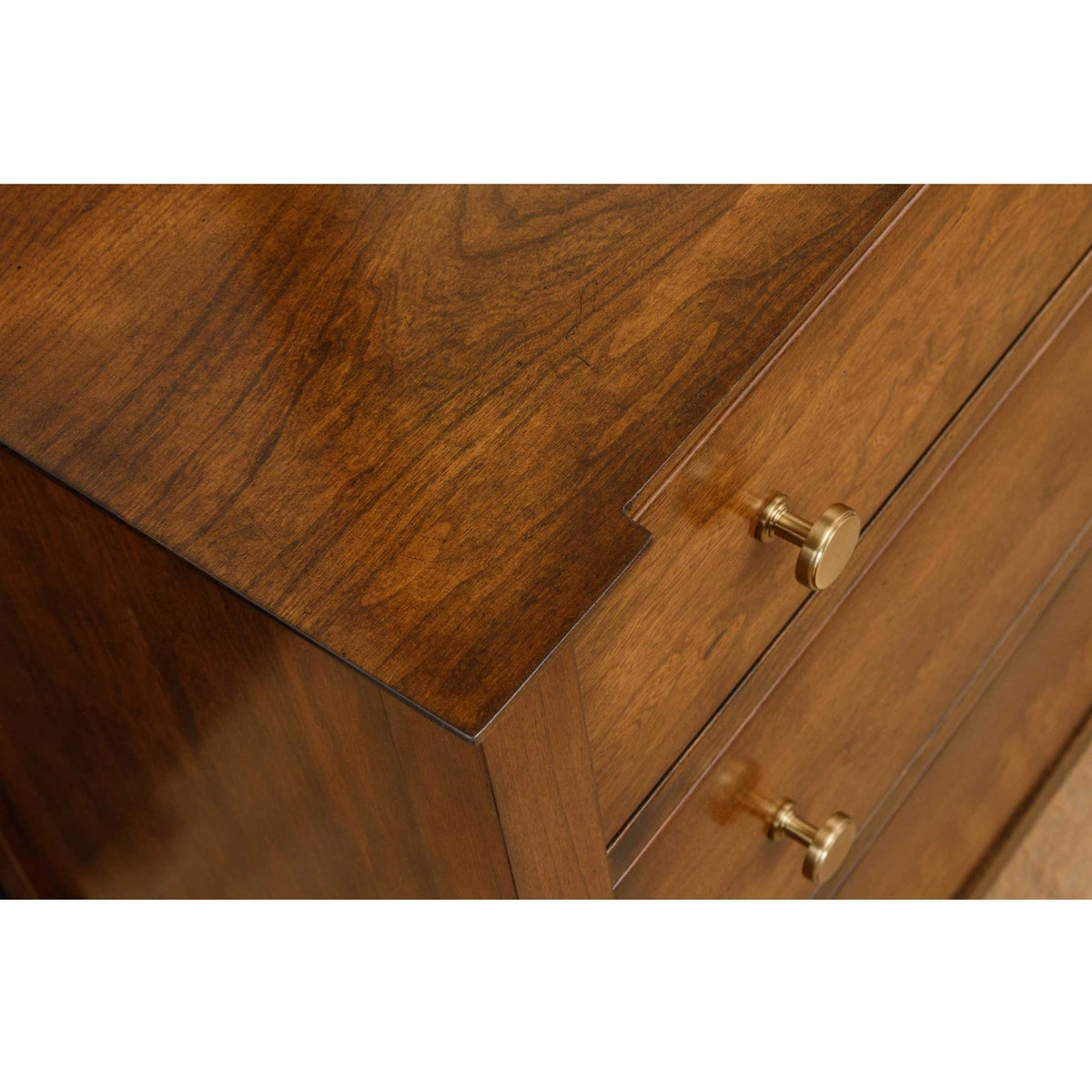 Top corner detail of the cherry night stand showing rich grain, stepped edge and two round brass knobs
