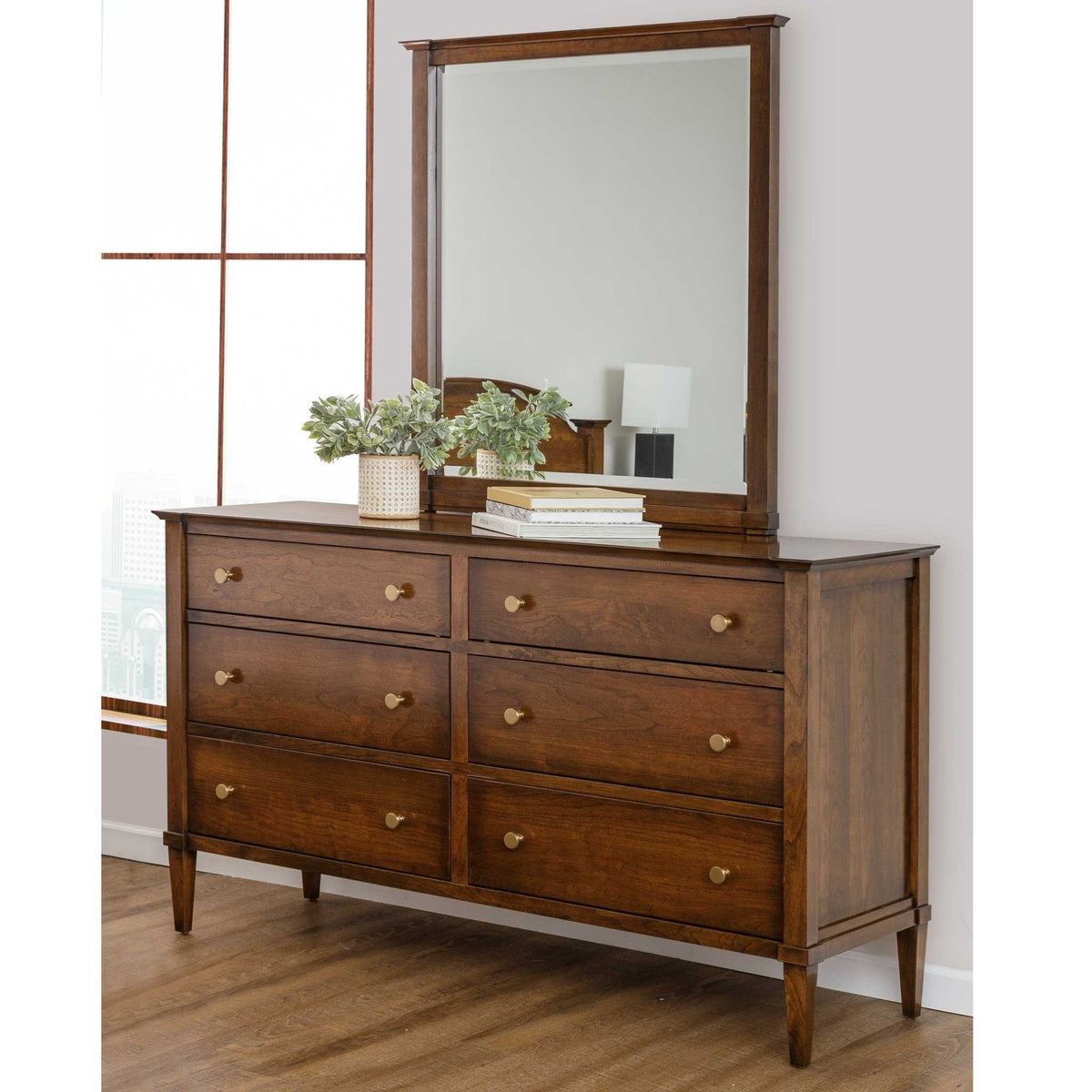 Cherry triple dresser with mirror styled with a plant and books, beside a window in a bright bedroom