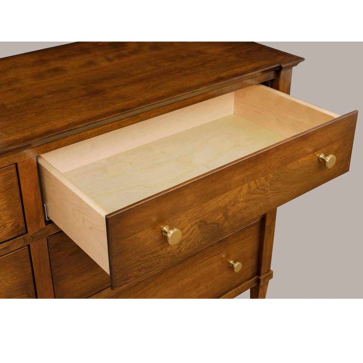 Nightstand drawer pulled open showing the wide maple-lined interior under the molded cherry top