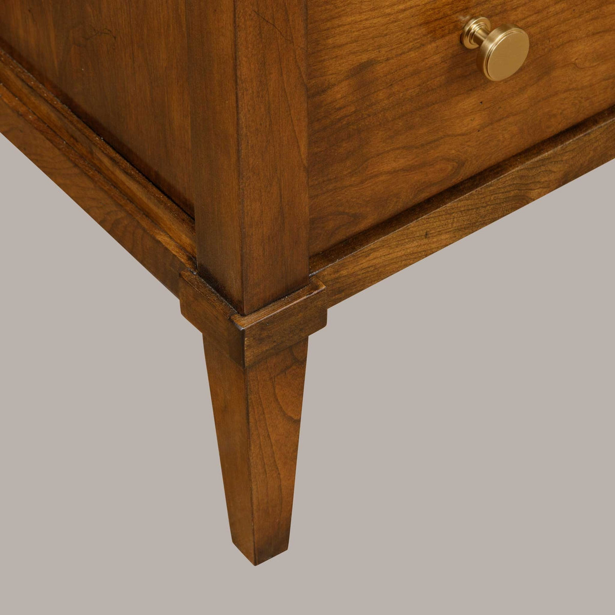 Tapered leg and lower corner detail of the solid cherry open night stand on a gray studio backdrop