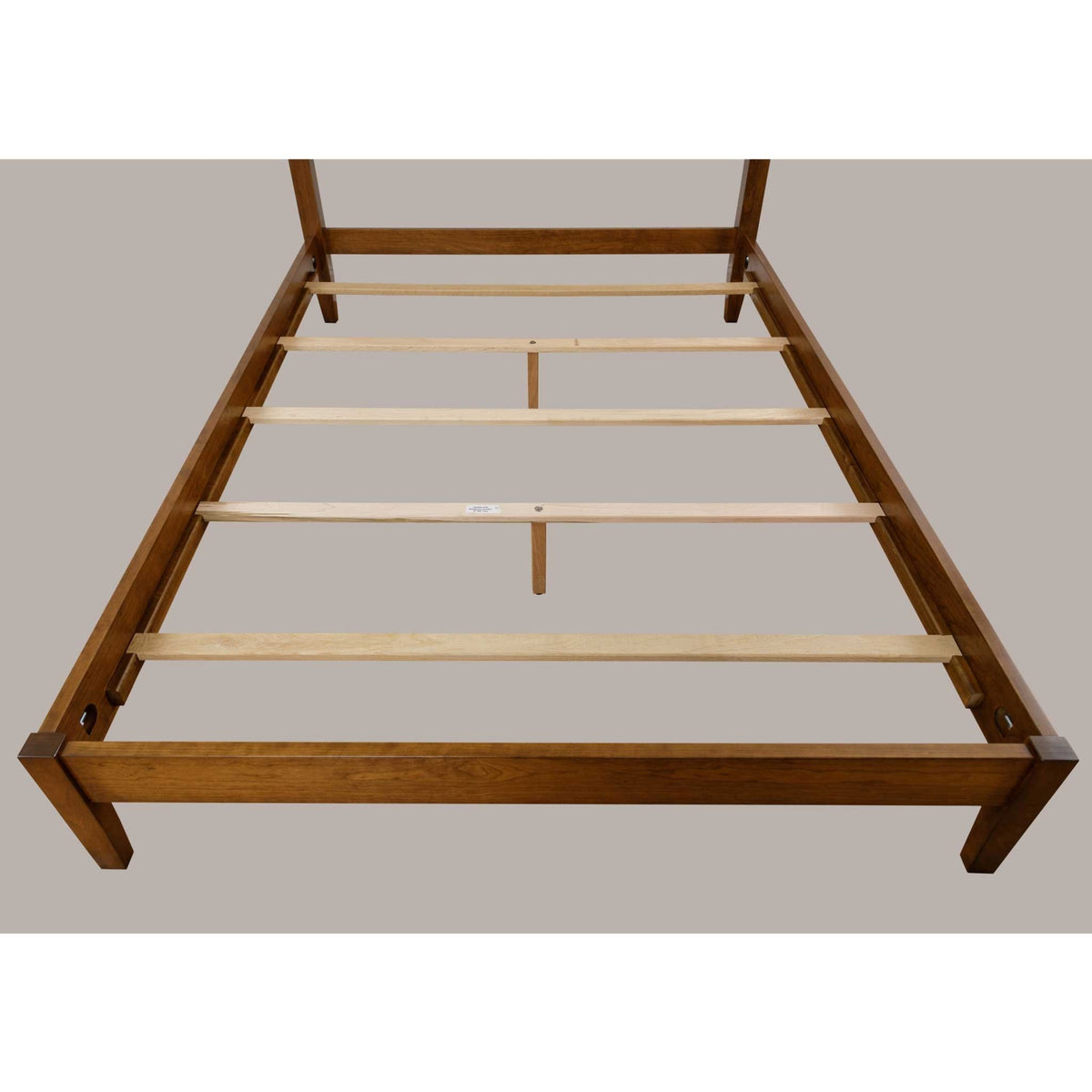 Cherry bed frame viewed from the foot showing pale maple slats and a center support leg between the rails