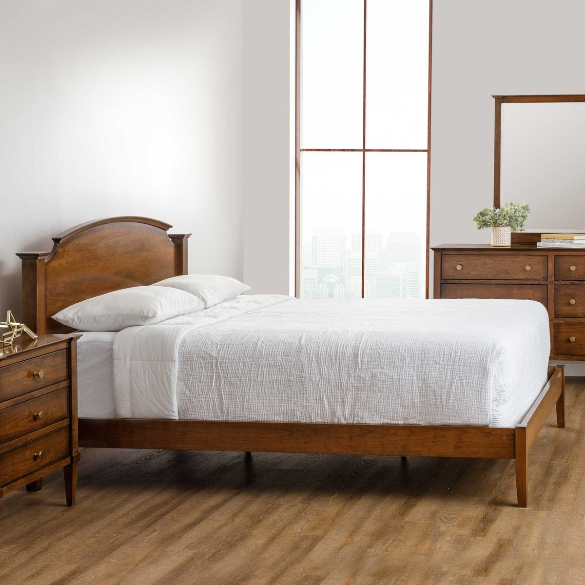 Cherry arched headboard bed with a low open footboard rail, white bedding, nightstand and mirrored dresser