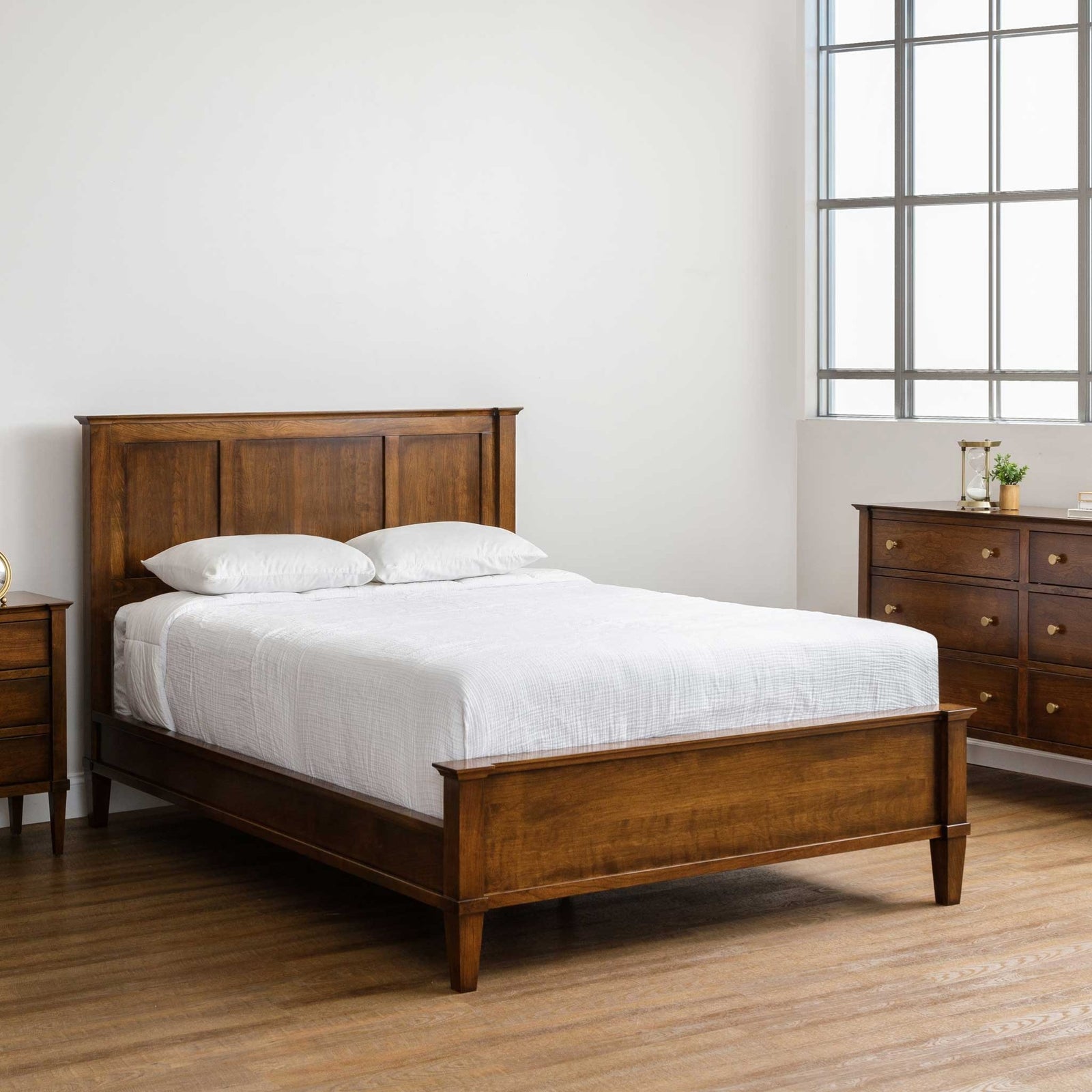 Cherry panel bed with a three-panel headboard and low footboard, dressed in white bedding beside a dresser and nightstand