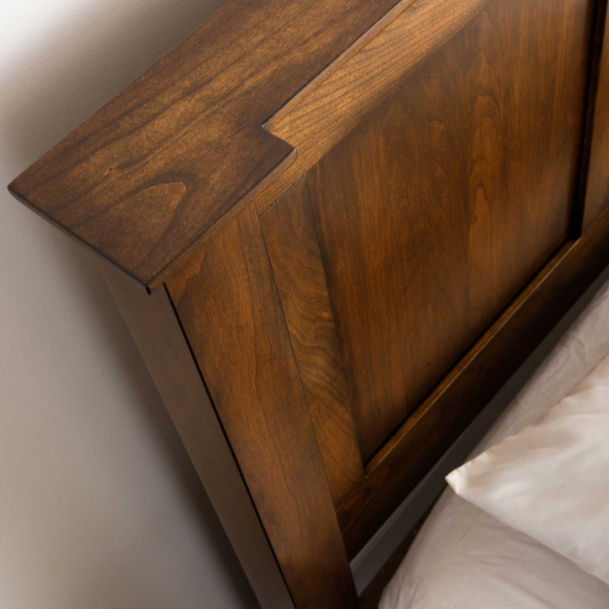 Corner detail of the low-footboard panel bed headboard, stepped cap and raised panel beside white pillows