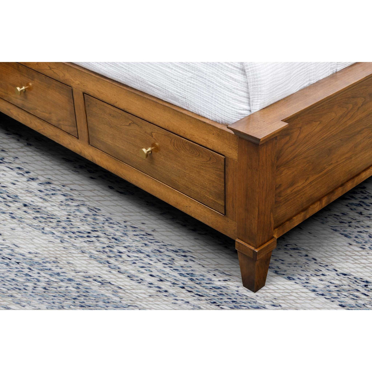 Footboard and side storage drawers of the cherry platform bed with brass knobs and square tapered feet on a blue rug