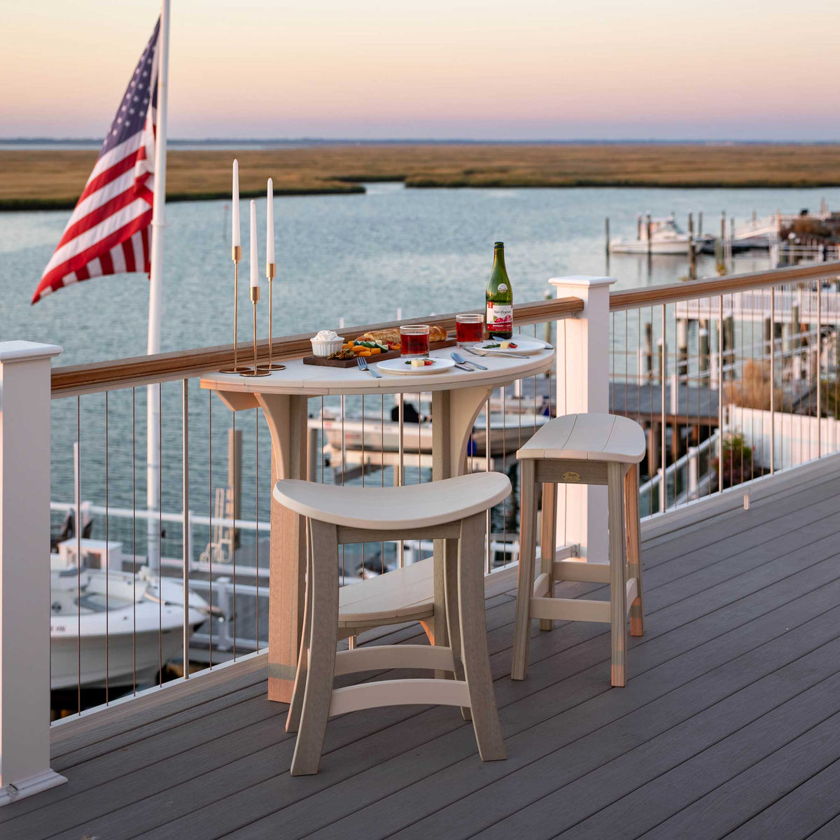 Sand colored half round bistro table with two saddle stools on a marina deck at sunset with a US flag