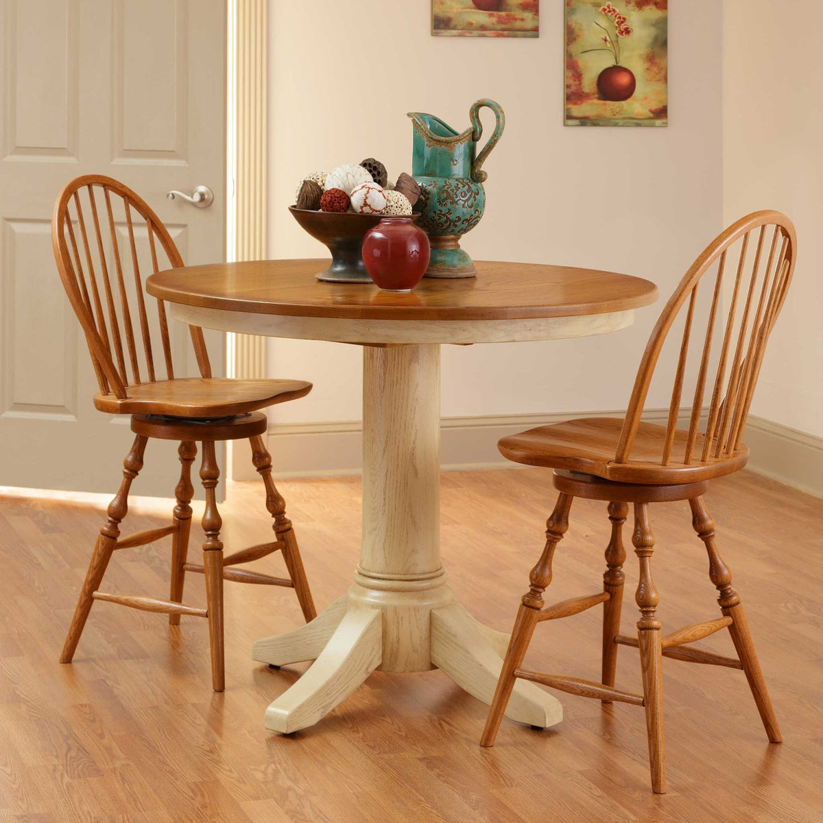 Round counter height table with an oak top and cream painted pedestal flanked by two oak swivel stools