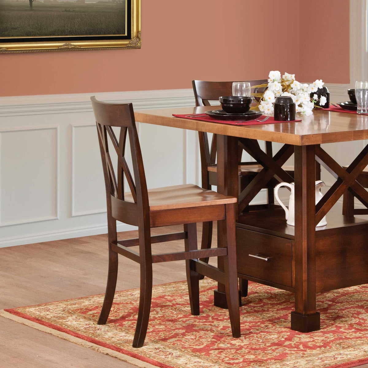 Double X back wood chairs pulled up to a two-tone dining table with a set place setting in a dining room