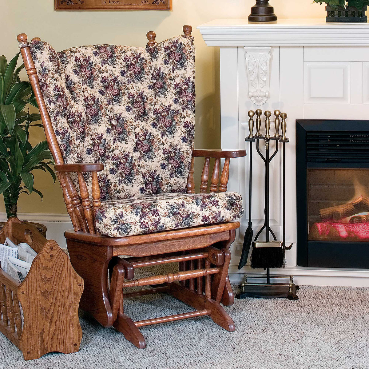 Angled view of the oak glider rocker with floral tapestry cushions by the fireplace showing the smooth glide rails