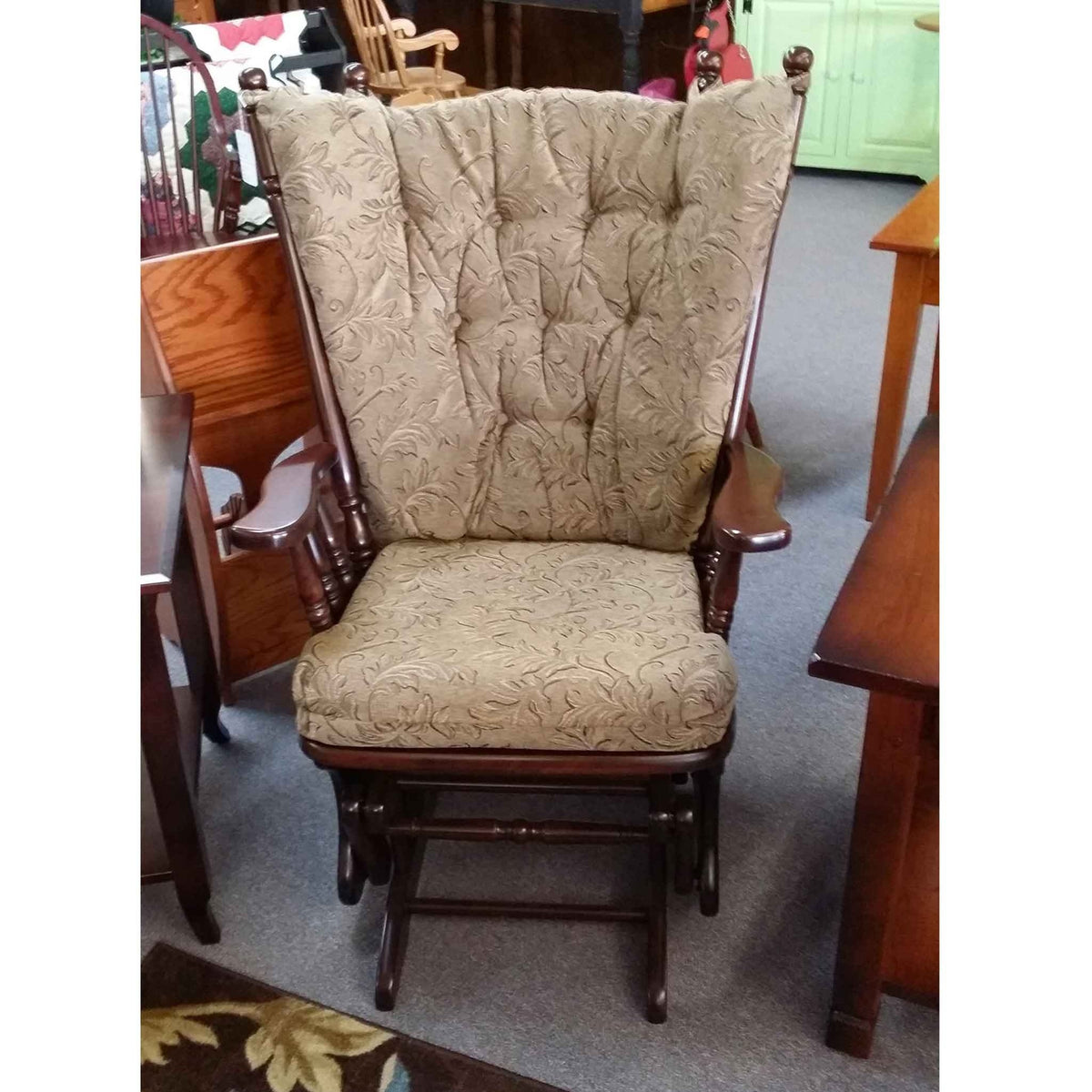 Dark cherry glider rocker with embossed sage leaf-pattern cushions shown in the furniture store showroom