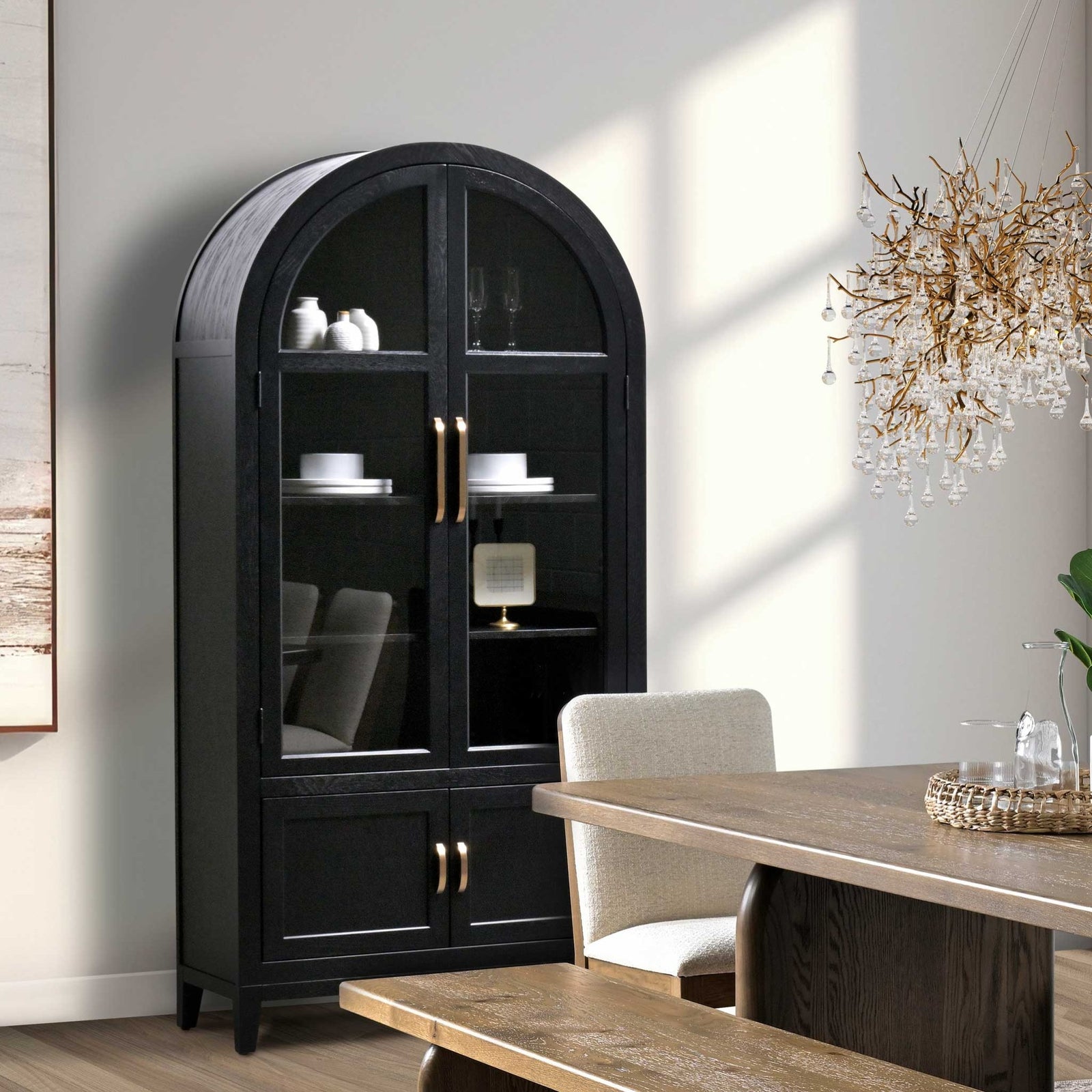 Black arched display cabinet with glass doors, three interior shelves, gold pulls and lower panel doors in a sunlit dining room