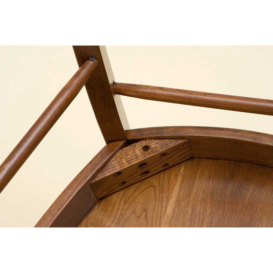 Underside corner of a wood chair seat showing the doweled corner block brace and turned stretchers