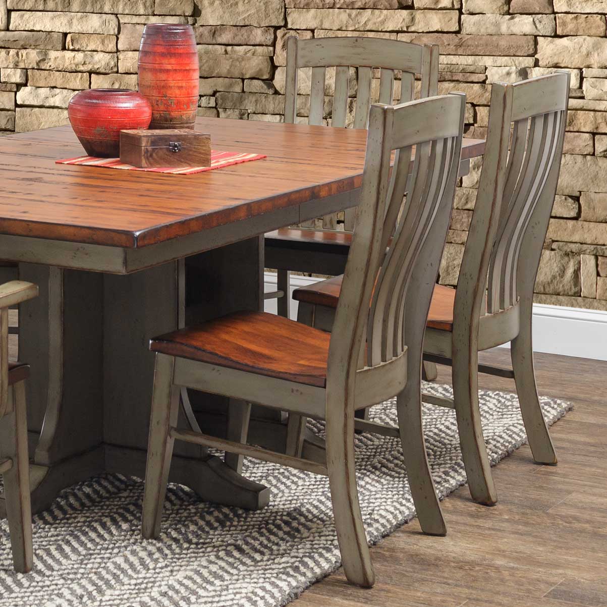 Sage green painted slat back dining chairs with stained wood seats around a two-tone pedestal dining table