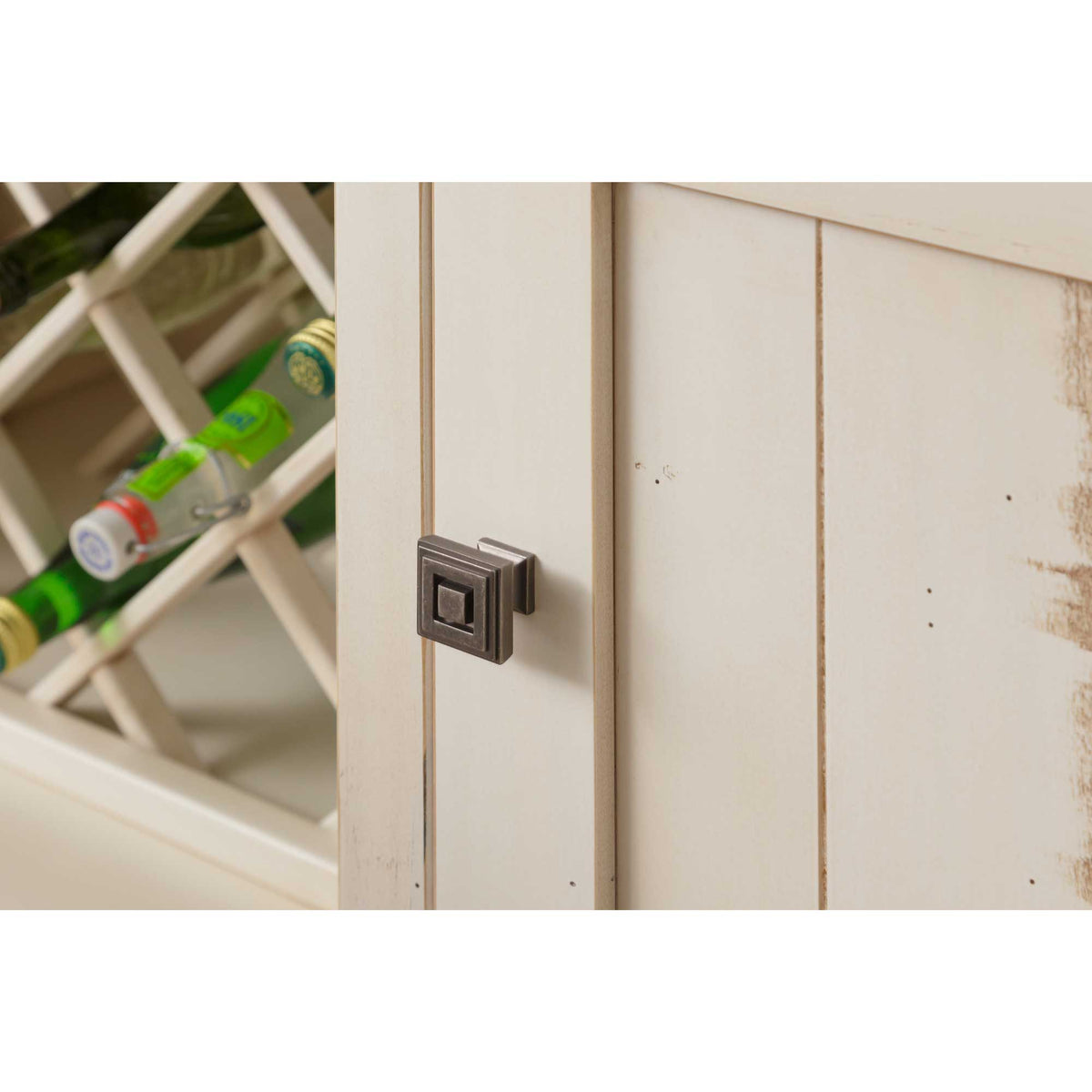 Detail of the distressed white cabinet door with a square pewter knob beside the wine bottle lattice