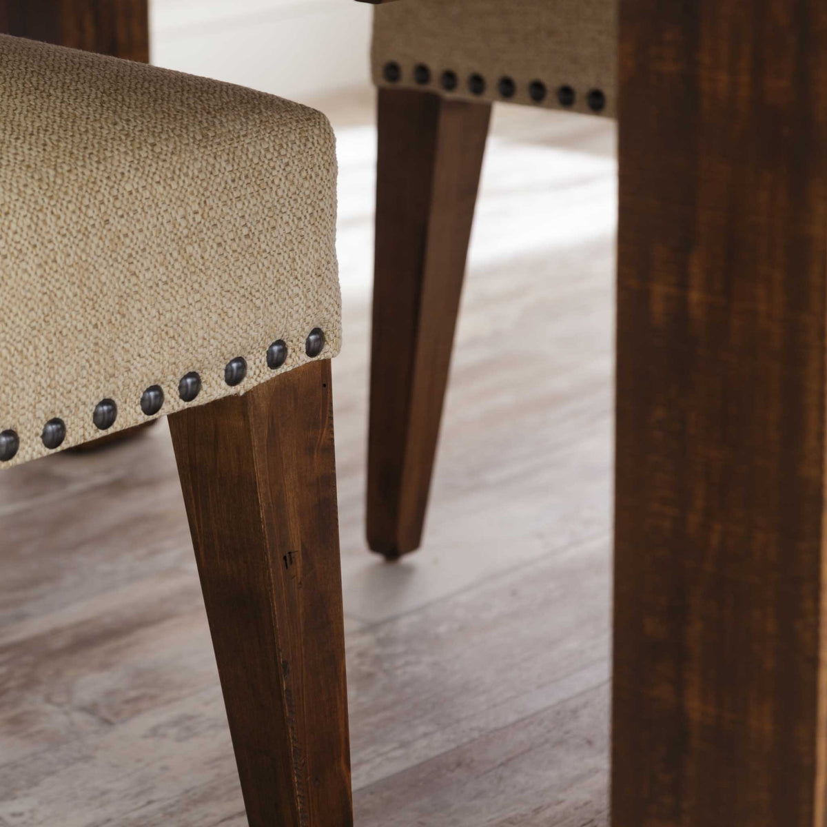 Close-up of a cream nailhead trimmed upholstered dining chair seat and rough sawn tapered wood legs