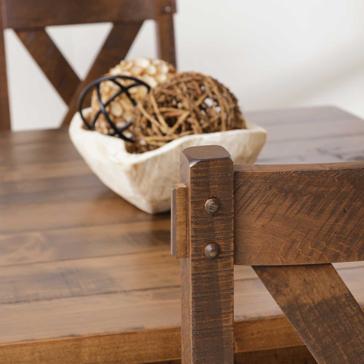 Detail of the rustic table's pegged leg bracket and plank top with a decorative bowl of spheres above
