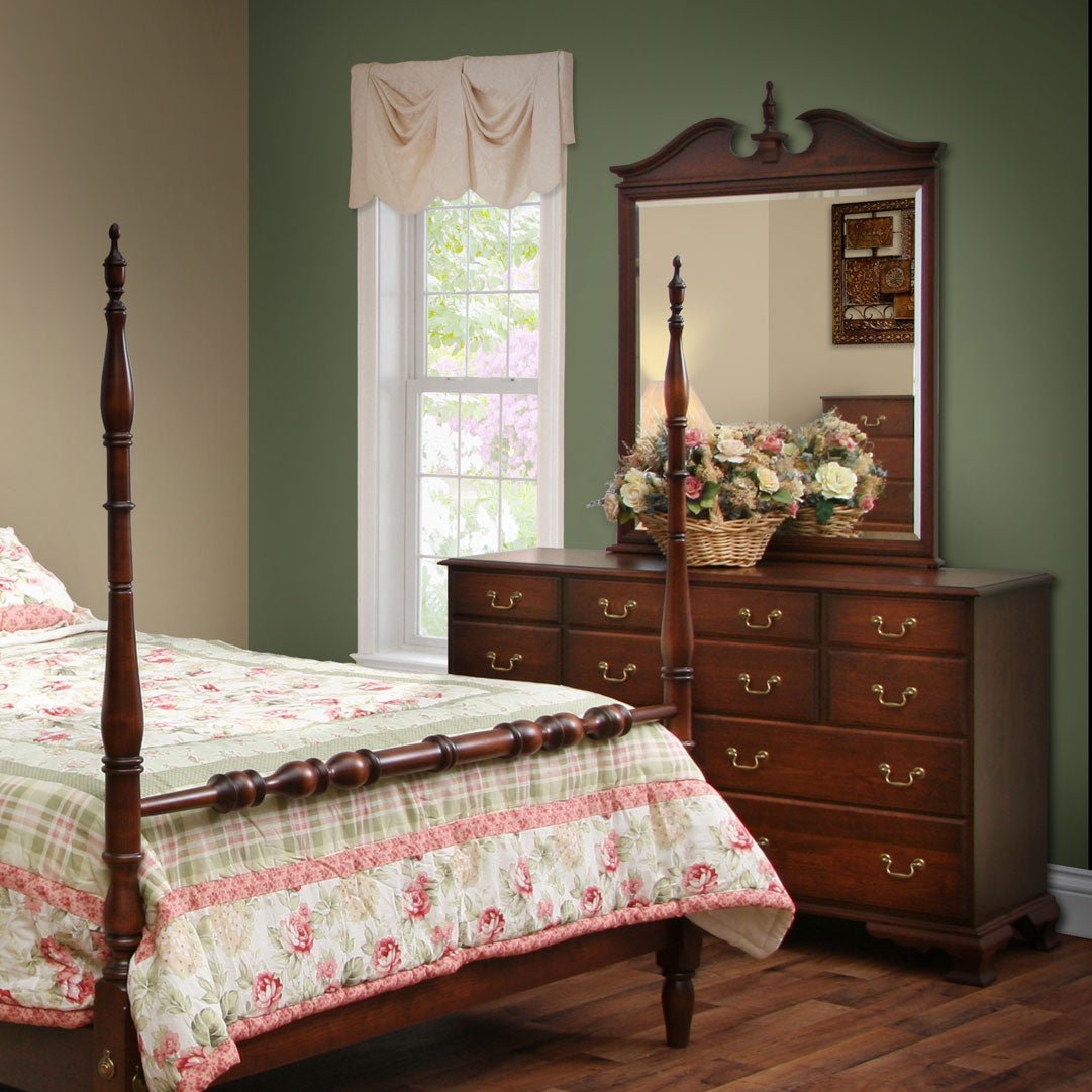 Turned-post cherry bed with a floral quilt beside a nine-drawer dresser topped by a broken-pediment mirror