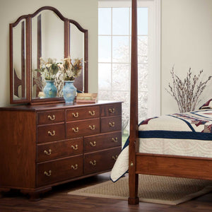 Cherry triple dresser with ten drawers and brass pulls, topped by an arched triview mirror and blue vases