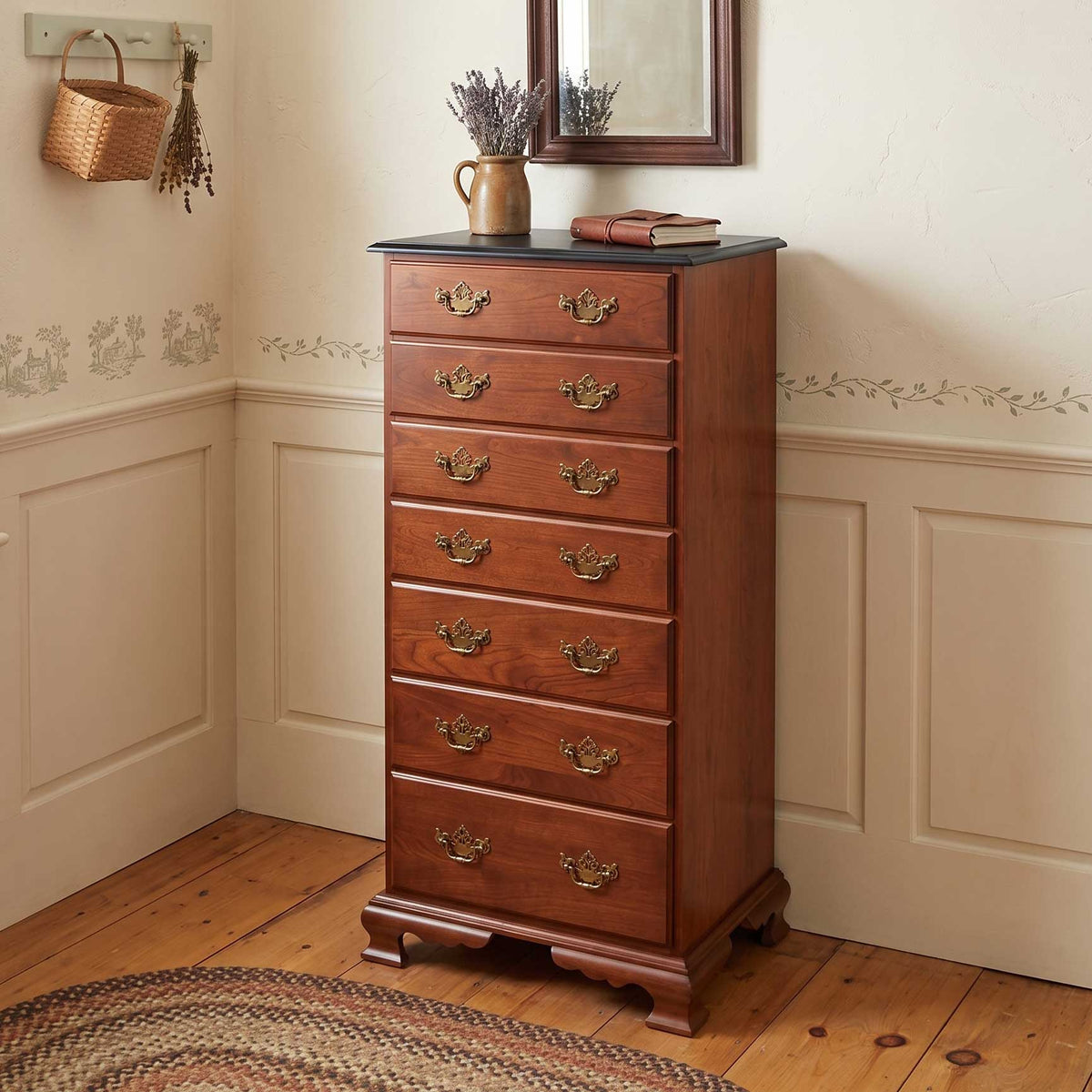 A tall wooden chest of drawers with eight drawers and ornate brass handles, styled in a traditional room corner with a dark tabletop and decorative items.