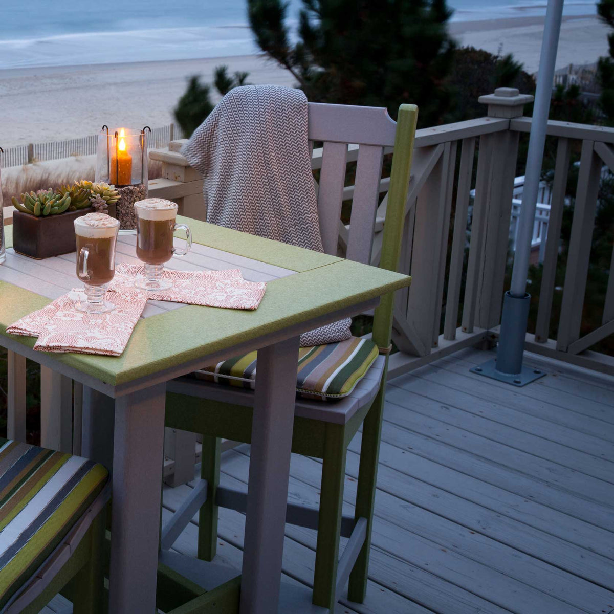 Lime green and gray poly bar height table with striped cushioned chairs on an oceanfront deck at dusk