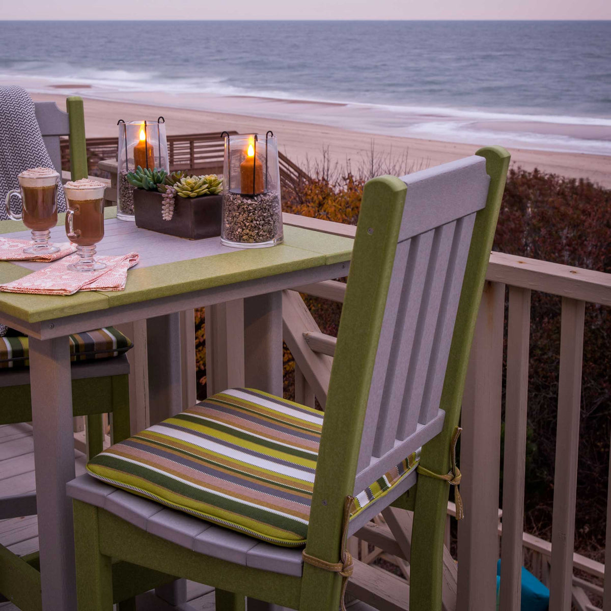 Green and gray poly bar chairs with striped seat cushions at a beachfront railing table with candles