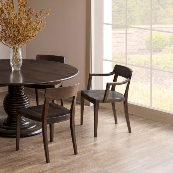 Modern wood dining chairs in dark walnut with curved crest rails and saddle seats around a round pedestal table
