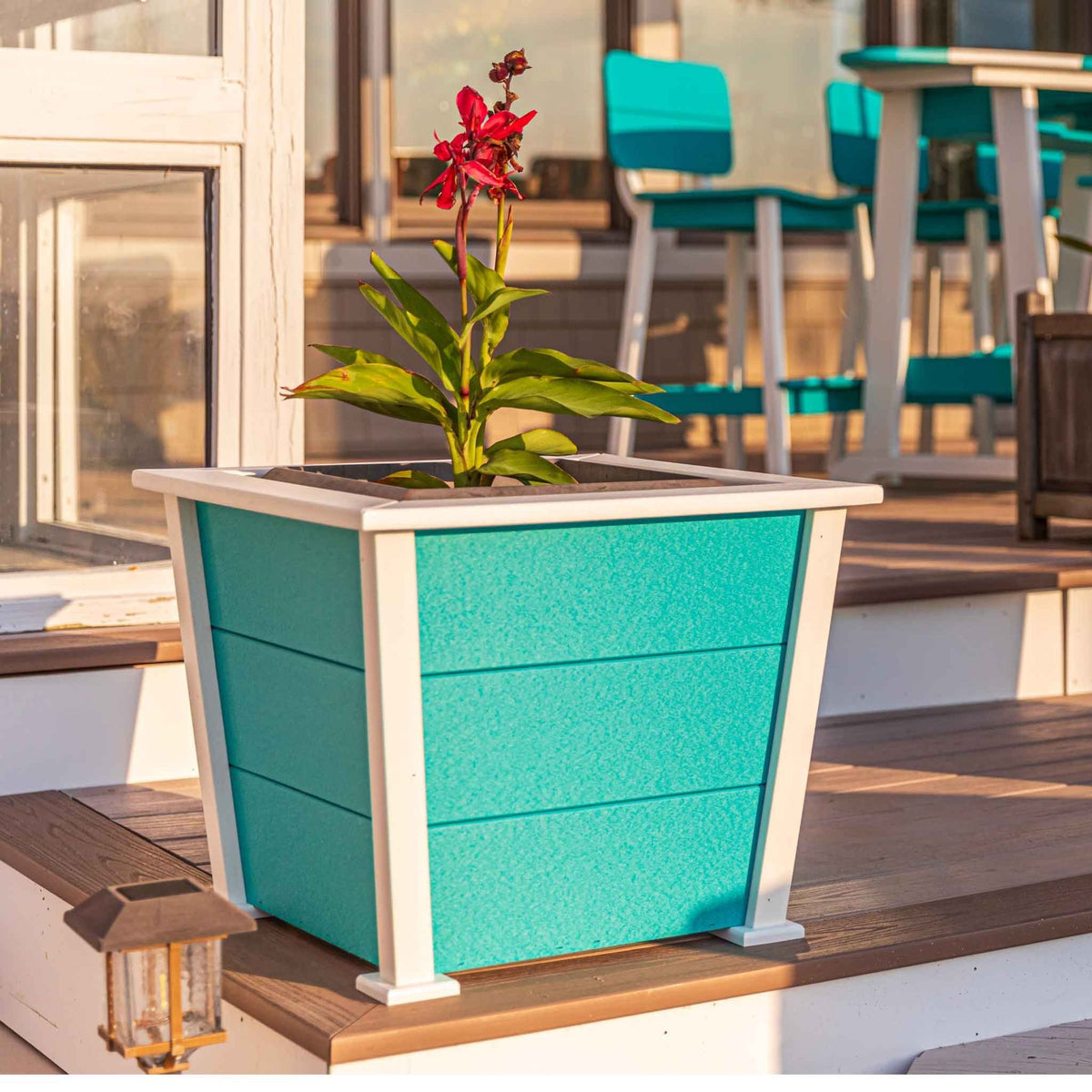 Turquoise and white tapered square poly planter with a flowering canna on a lakeside deck at sunset