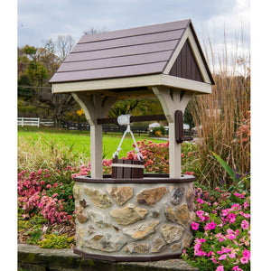 Large stone wishing well with brown poly roof, tan posts, rope bucket and crank handle, surrounded by pink and coral flowers