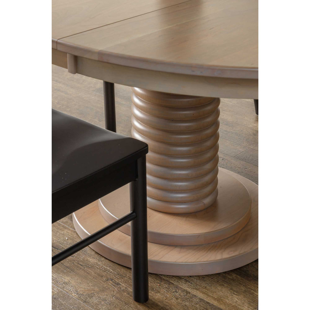 Close-up of the round table's ribbed pedestal column and tiered base beside a black wood dining chair